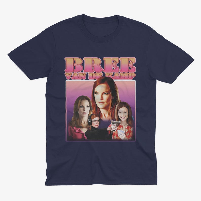 May include: Navy blue t-shirt with a retro-style graphic of Bree Van de Kamp from the TV show Desperate Housewives. The graphic features Bree and other characters from the show in a pink and purple background.