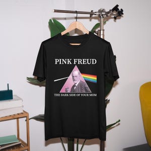 May include: Black t-shirt with a pink triangle and the text "PINK FREUD" and "THE DARK SIDE OF YOUR MOM". The triangle contains a picture of Sigmund Freud.