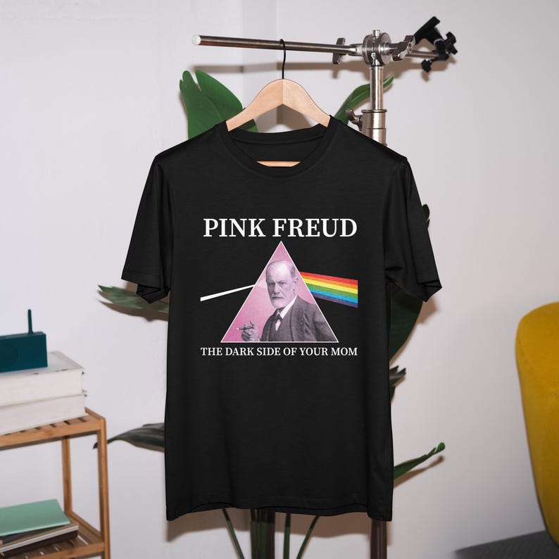 May include: Black t-shirt with a pink triangle and the text "PINK FREUD" and "THE DARK SIDE OF YOUR MOM". The triangle contains a picture of Sigmund Freud.