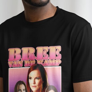 May include: Black t-shirt with a pink and yellow graphic print that says "Bree Van de Kamp". The graphic also features a woman with long brown hair.