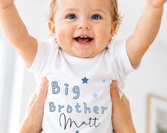 May include: A white short-sleeved t-shirt featuring the blue text "Big Brother Matt" printed on the front. The design includes small blue and light blue star graphics scattered around the lettering. The shirt has a simple crew neckline.