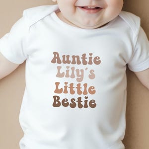 Neutral-toned personalised baby vest with retro-style "Auntie's Little Bestie" design, perfect for gifting from aunties to newborns.