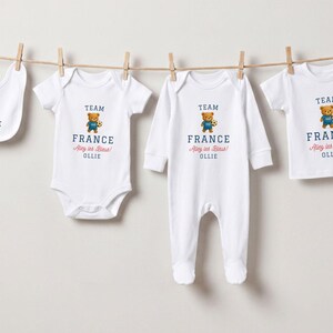 a collection of four white baby clothes, each with a teddy bear printed on them, hanging on a clothesline.