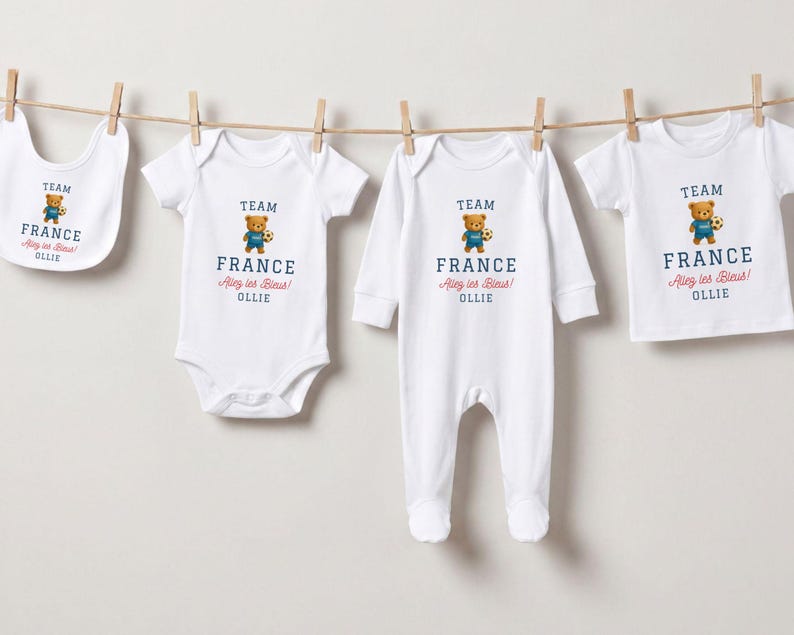 a collection of four white baby clothes, each with a teddy bear printed on them, hanging on a clothesline.