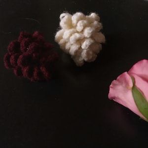 May include: Three crocheted flower shapes in burgundy, white, and pink. The flowers are on a black surface.