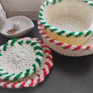 Può includere: Tre ciotole all'uncinetto con strisce rosse e verdi. Le ciotole sono annidate l'una dentro l'altra, con la ciotola più grande in basso e la più piccola in alto.