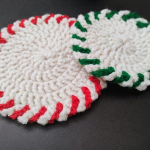 May include: Two crocheted coasters with a white centre and a red and green striped border. The coasters are made with a soft, textured yarn.