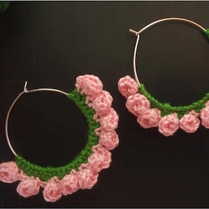 May include: A pair of hoop earrings with pink crocheted flowers and green leaves around the hoop.