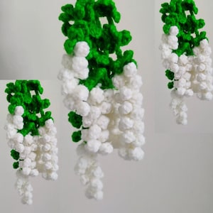 May include: Three crocheted flower garlands with green leaves and white blossoms. The garlands are hanging from the top of the image.