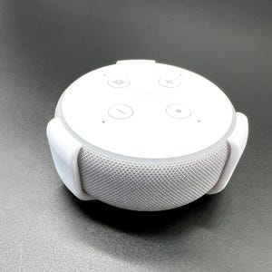 Könnte beinhalten: Weißer intelligenter Lautsprecher mit vier Knöpfen oben. Die Knöpfe sind mit Symbolen für Lautstärke erhöhen, Lautstärke verringern, Wiedergabe/Pause und Mikrofon stumm schalten beschriftet.