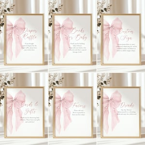May include: Set of six framed signs with gold borders, featuring a watercolor pink bow design. Each sign has a different message in elegant script, including "Diaper Raffle," "Books for Baby," and "Custom Sign," perfect for a baby shower.
