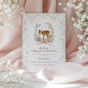 Może przedstawiać: Zaproszenie na baby shower z ilustracją sarny w kwiatowym łuku. Tekst brzmi "oh deer a baby girl is almost here" ze szczegółami wydarzenia, w tym datą, godziną i miejscem, w miękkiej, pastelowej kolorystyce.