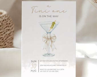 Puede incluir: Tarjeta de invitación de color beige claro con el texto "Tini one is on the way". Ilustración en acuarela de una copa de martini con aceitunas y un lazo. La fecha es el 30 de agosto.