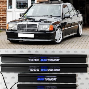 以下が含まれることがあります： 黒いメルセデス・ベンツ190Eセダン、サンルーフ付き。 下には、青色で「190E evolution」と書かれた4つの黒いドアシルがあります。 車はレンガ造りの建物の前に駐車されています。