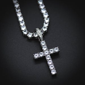 May include: A silver chain necklace with a silver cross pendant, both encrusted with clear cubic zirconia stones.