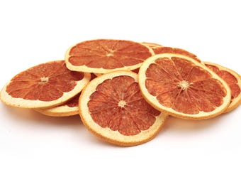 May include: A small pile of dehydrated grapefruit slices. Each circular slice features a deep reddish-pink interior with a visible radial segment pattern and a thin, light-coloured rind. The texture appears dry and firm with a matte finish.