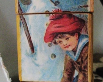 May include: A vintage Christmas card featuring a snowman wearing a brown hat and a child in a red hat and sailor shirt holding a shovel.