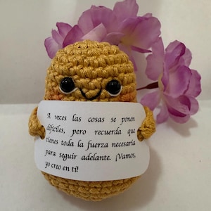 Peut inclure: Un personnage jaune en crochet tenant une carte blanche avec le texte "A veces las cosas se ponen dificiles, pero recuerda que tienes toda la fuerza necesaria para seguir adelante. ¡Vamos, yo creo en tí!"