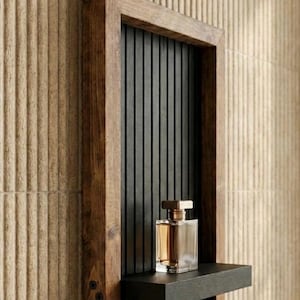 Può includere: Una mensola a muro con cornice in legno con interno nero e una piccola mensola. Un flacone di profumo trasparente con tappo dorato è posto sulla mensola. La cornice è in legno scuro ed è montata su una parete beige strutturata.