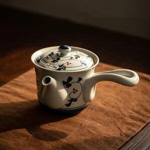 Handbeschilderde kyusu theepot met zijhandvat en filter.