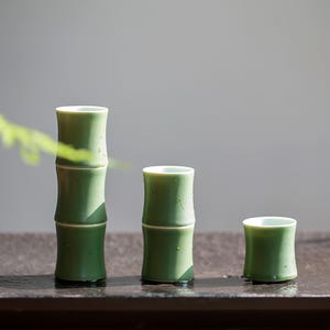 Può includere: Tre tazze da tè in ceramica verde con un design a bambù. Le tazze sono impilate l'una sull'altra, con la tazza più grande in basso e la tazza più piccola in alto.
