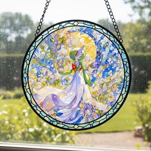 Puede incluir: Vidriera redonda que representa un personaje de Gardevoir con un vestido blanco fluido, sobre un fondo de flores y una luna creciente. La obra de arte está enmarcada en negro con una cadena para colgar.