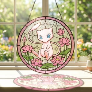 Może przedstawiać: Okrągłe witrażowe okno z różową postacią z kreskówki z niebieskimi oczami, otoczone różowymi kwiatami lotosu i zielonymi liśćmi. Grafika jest oprawiona w różową ramkę i zawieszona na łańcuchu.