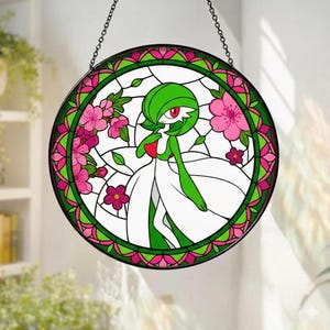 Może przedstawiać: Okrągłe witraż przedstawiający zielono-białą postać z czerwonym okiem, otoczoną różowymi kwiatami i zielonymi liśćmi. Obramowanie jest zielono-różowe, z czarnym łańcuchem do zawieszenia. Element dekoracyjny.