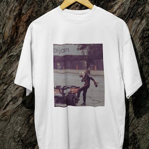 May include: White t-shirt with a graphic print of a race car driver celebrating on a racetrack. The text "aijan" is visible in the background.