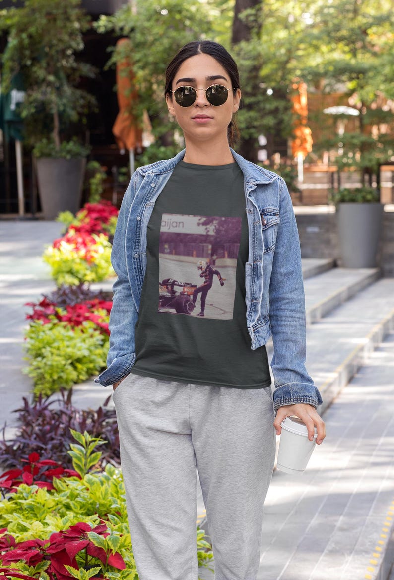 May include: A dark gray t-shirt with a graphic print of a person riding a small motorcycle. The graphic is in a vintage style and includes the word "aijan".