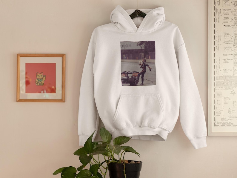 K&ouml;nnte beinhalten: Wei&szlig;er Hoodie mit einem Grafikdruck einer Person in schwarzer Kleidung, die vor einem Geb&auml;ude mit dem Wort "Bijan" steht.