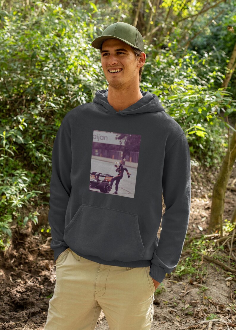 K&ouml;nnte beinhalten: Ein dunkelgrauer Kapuzenpullover mit einem Grafikdruck einer Person in einem Rennanzug, die einen Reifen tritt. Der Text "aijan" ist auf dem Grafikdruck gedruckt.