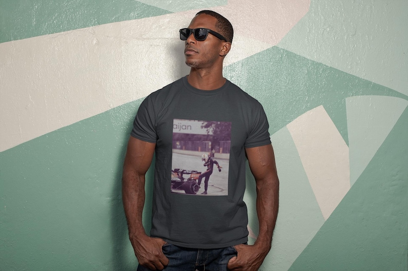 May include: A man wearing a dark gray t-shirt with a vintage photo of a person in a racing suit and a car. The photo has the word "Bijan" printed on it.
