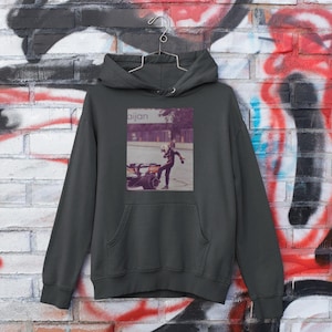 K&ouml;nnte beinhalten: Ein dunkelgrauer Kapuzenpullover mit einem Grafikdruck einer Person, die ein Motorrad f&auml;hrt. Die Grafik ist im Vintage-Stil gehalten und tr&auml;gt den Text "Bijan".