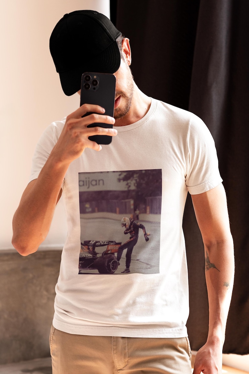 May include: A white t-shirt with a black and white photo of a race car driver on the front. The photo shows the driver in a racing suit, standing next to a race car. The text "aijan" is visible in the background.