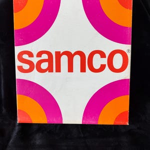 Może przedstawiać: Białe pudełko z czerwonym logo "samco" i wzorem koncentrycznych kół w kolorze różowym i pomarańczowym.