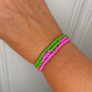 May include: A bracelet made of pink and green beads. The bracelet is worn on a person's wrist.