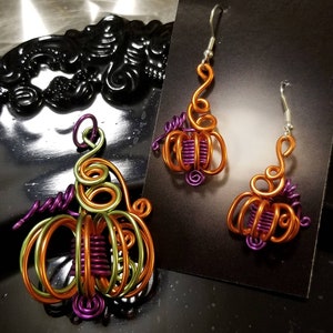 May include: A pair of pumpkin-shaped earrings and a pendant made of wire wrapped in orange, green, and purple wire. The earrings and pendant are handmade and have a whimsical design.