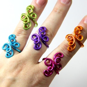 May include: Four colorful wire rings with a butterfly design. The rings are in shades of green, purple, orange, and pink.