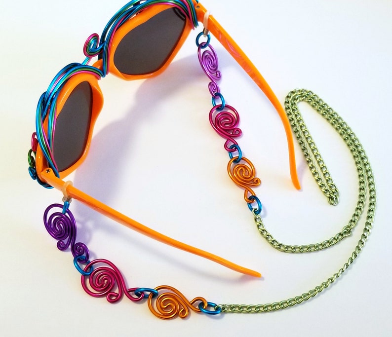May include: Orange sunglasses with a colorful wire frame and a chain with colorful wire swirls. The chain is attached to the sunglasses with a metal loop.