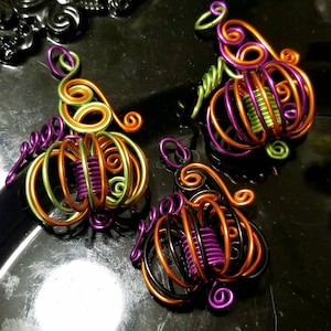 May include: Three wire-wrapped pumpkin ornaments in orange, green, and black with purple accents.
