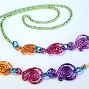 May include: A colorful eyeglass chain with a green chain and four decorative swirls in orange, blue, pink, and purple.