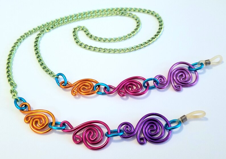 May include: A colorful eyeglass chain with a green chain and four decorative swirls in orange, blue, pink, and purple.