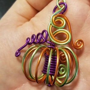 May include: A wire-wrapped pumpkin charm with green, orange, and purple wire. The charm is shaped like a pumpkin with a stem and leaves.