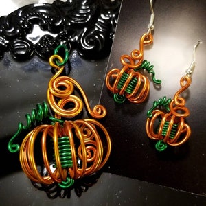 May include: A set of wire pumpkin earrings and a necklace. The earrings and necklace are made of copper wire and green wire. The pumpkins are detailed with swirls and loops.