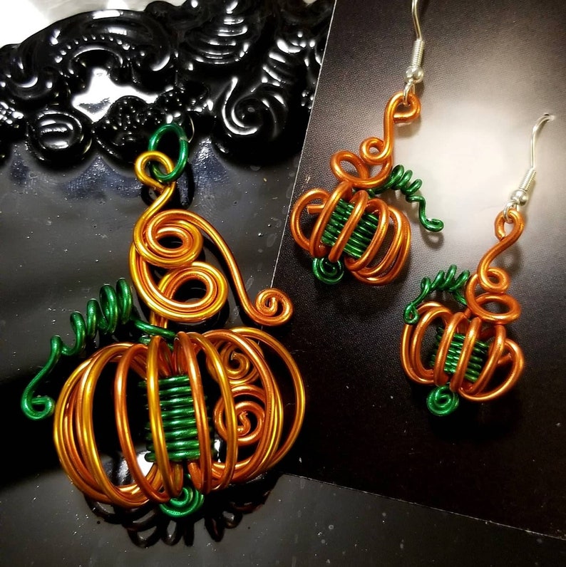 May include: A set of wire pumpkin earrings and a necklace. The earrings and necklace are made of copper wire and green wire. The pumpkins are detailed with swirls and loops.