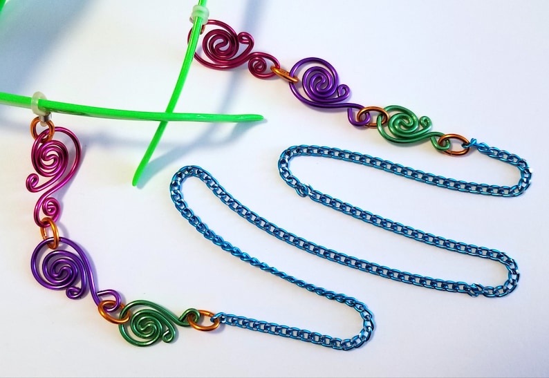 May include: A turquoise chain with colorful wire swirls attached to each end. The swirls are in shades of pink, purple, green, and orange.