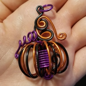 May include: A wire-wrapped pumpkin charm with a purple stem, black and orange stripes, and a purple center.