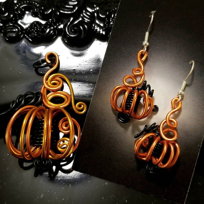 May include: A pair of pumpkin-shaped earrings made of wire. The earrings are orange and black and have a dangling design.