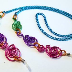 May include: A colorful glasses chain with a turquoise chain and multiple swirls of green, purple, and pink metal.
